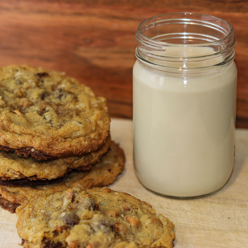 Stack of 3 cookies next to a glass of milk. One cookie placed on the table in front of both.