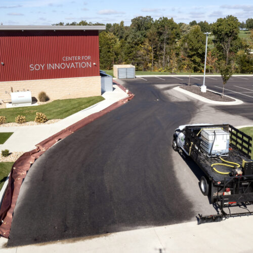 A Truck Applying RePlay Is An Agricultural Oil Seal And Preservation Agent To The Asphalt In Front Of The Center For Soy Innovation Building