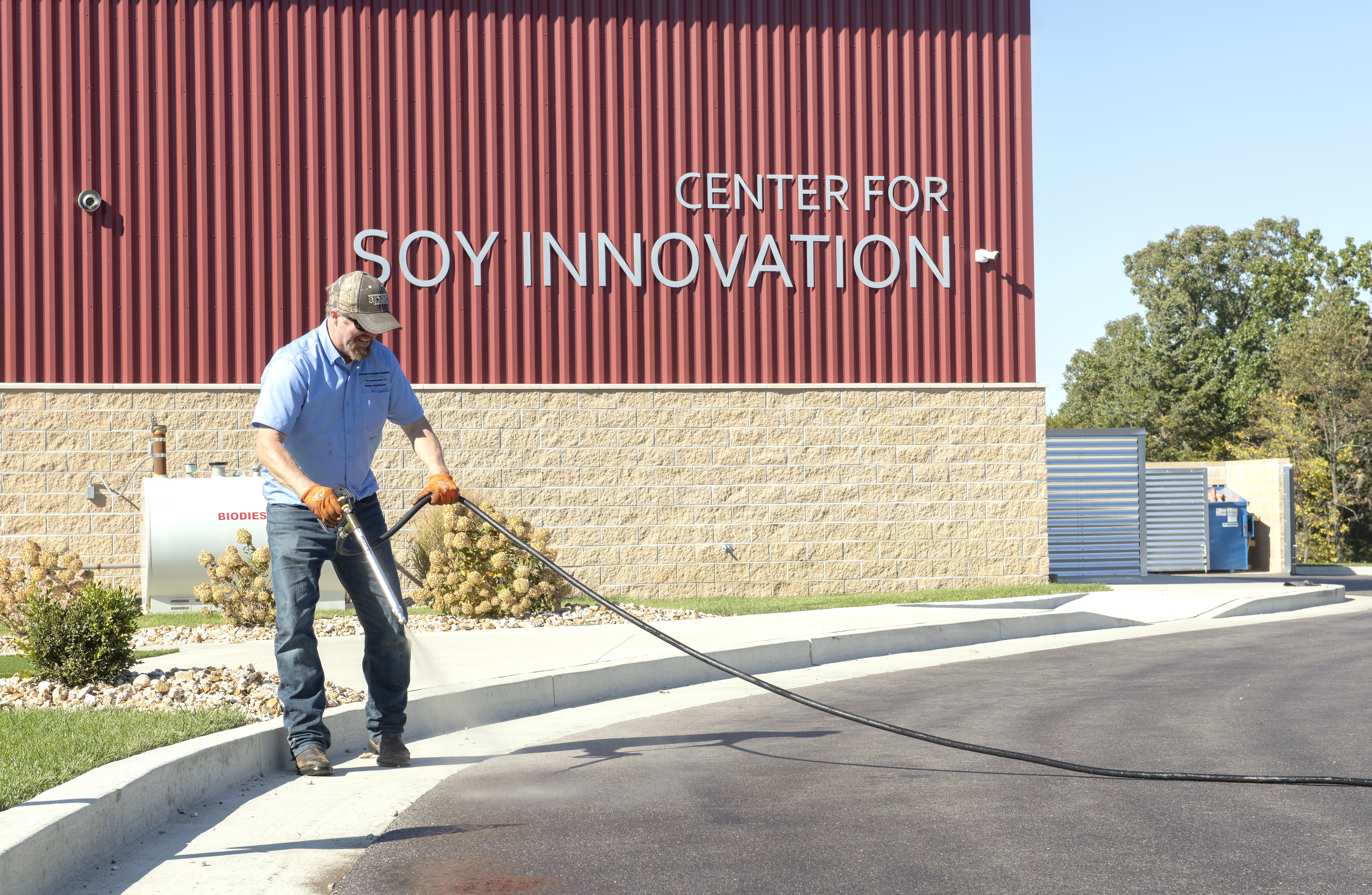 A man applying RePlay is an agricultural oil seal and preservation agent to the asphalt in front of the Center for Soy Innovation Building